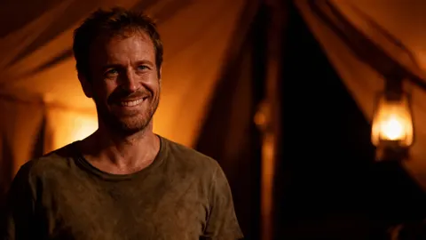 Still from No Splash: a smiling man in a lamplit tent