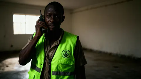 Still from No Splash: an aid worker in a hi-vis vest on the phone in a dark room