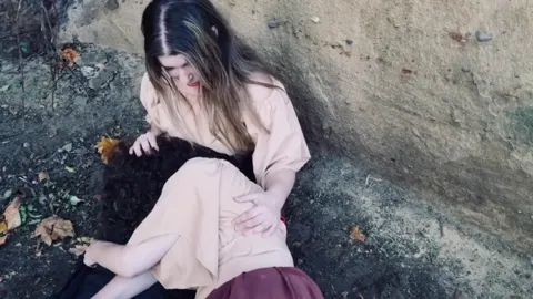 Still from Trapped in Their Dreams: a woman slumped against a stone wall